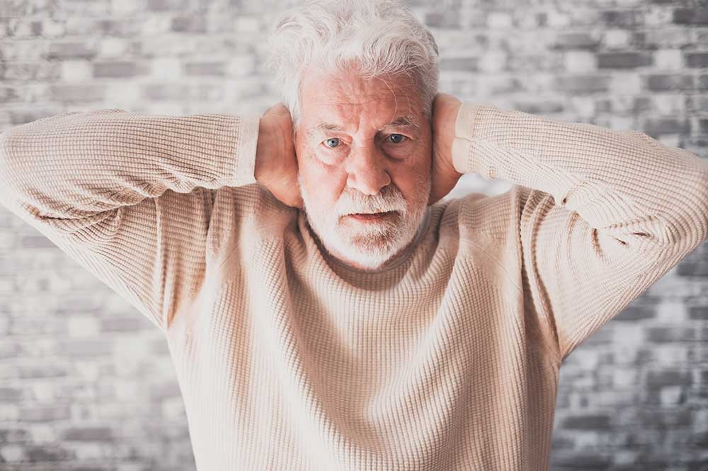 White-haired man in a cream sweater pressing his hands over ears that feel clogged, from Audiology Concepts in Edina and across Minnesota